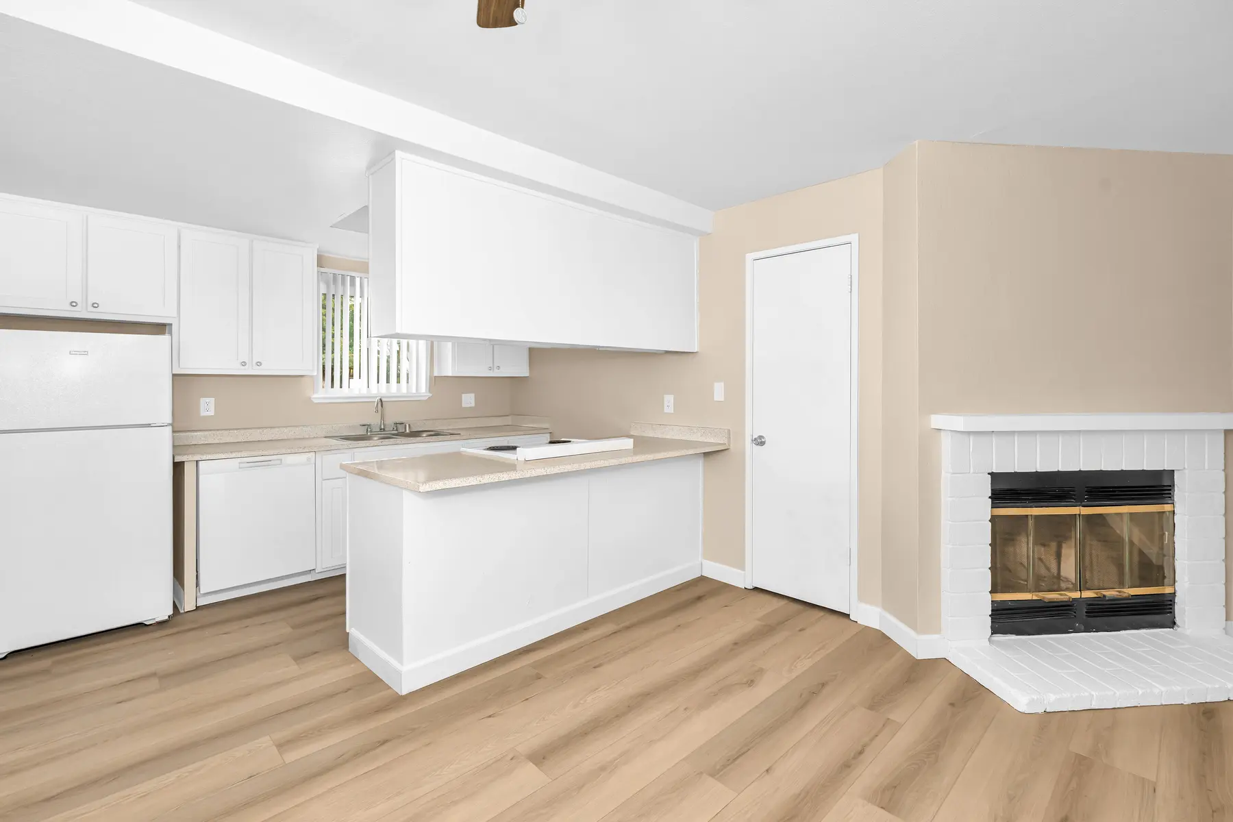 Bright and airy kitchen featuring white cabinets, a small island, and a fireplace on a beige wall.