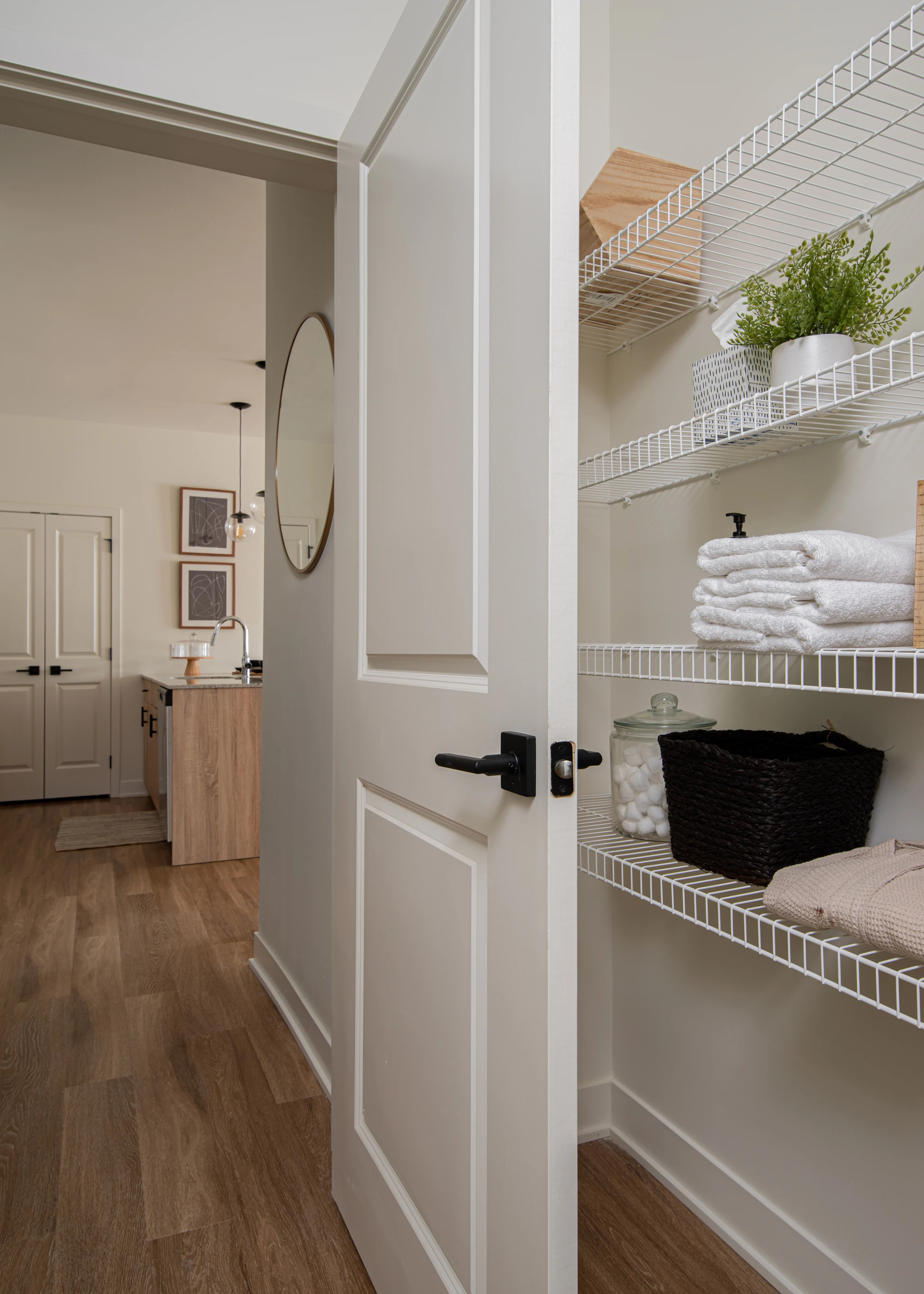 A view through an open door into a well-organized closet showcasing shelves with neatly arranged towels, a basket, and decorative plants, next to a bathroom area.