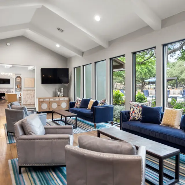 A spacious modern living area with large windows, comfortable seating, and a combination of wooden and plush furniture with decorative pillows.