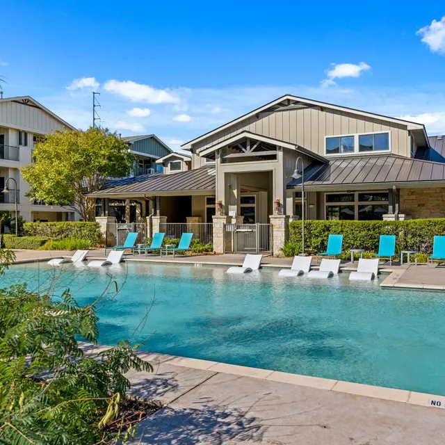 Modern apartment complex pool area with lounge chairs and clubhouse.