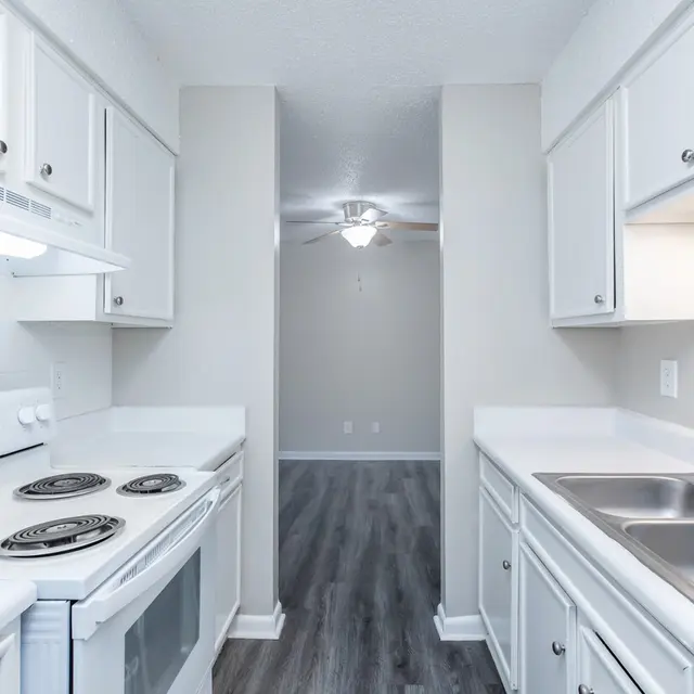 A modern kitchen with white cabinets, a stove, and a double sink, with a view into a well-lit room beyond.