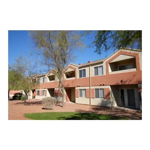 View of a multi-unit apartment building with a landscaped yard and clear blue sky.