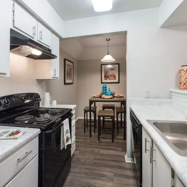 Cozy kitchen featuring black appliances, white cabinets, marble countertops, and a dining area with a table and chairs.