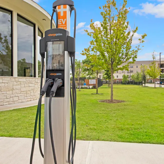 Electric Vehicle Charging Station An electric vehicle charging station on a grassy area with trees in the background and a building to the left.