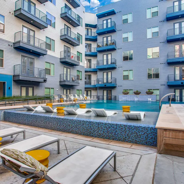 A stylish apartment complex pool area featuring a modern design with lounge chairs and vibrant yellow accents.