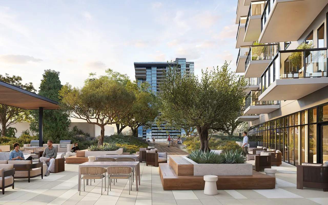 A modern outdoor space featuring comfortable seating arrangements, trees, and a view of nearby buildings. The design includes wooden furniture and a landscaped area with greenery.