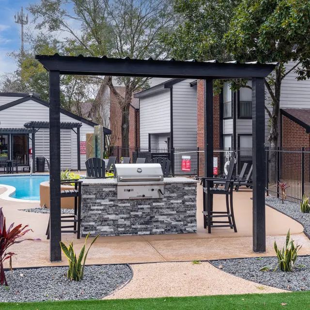 An outdoor grilling area with a built-in grill and seating near a swimming pool.