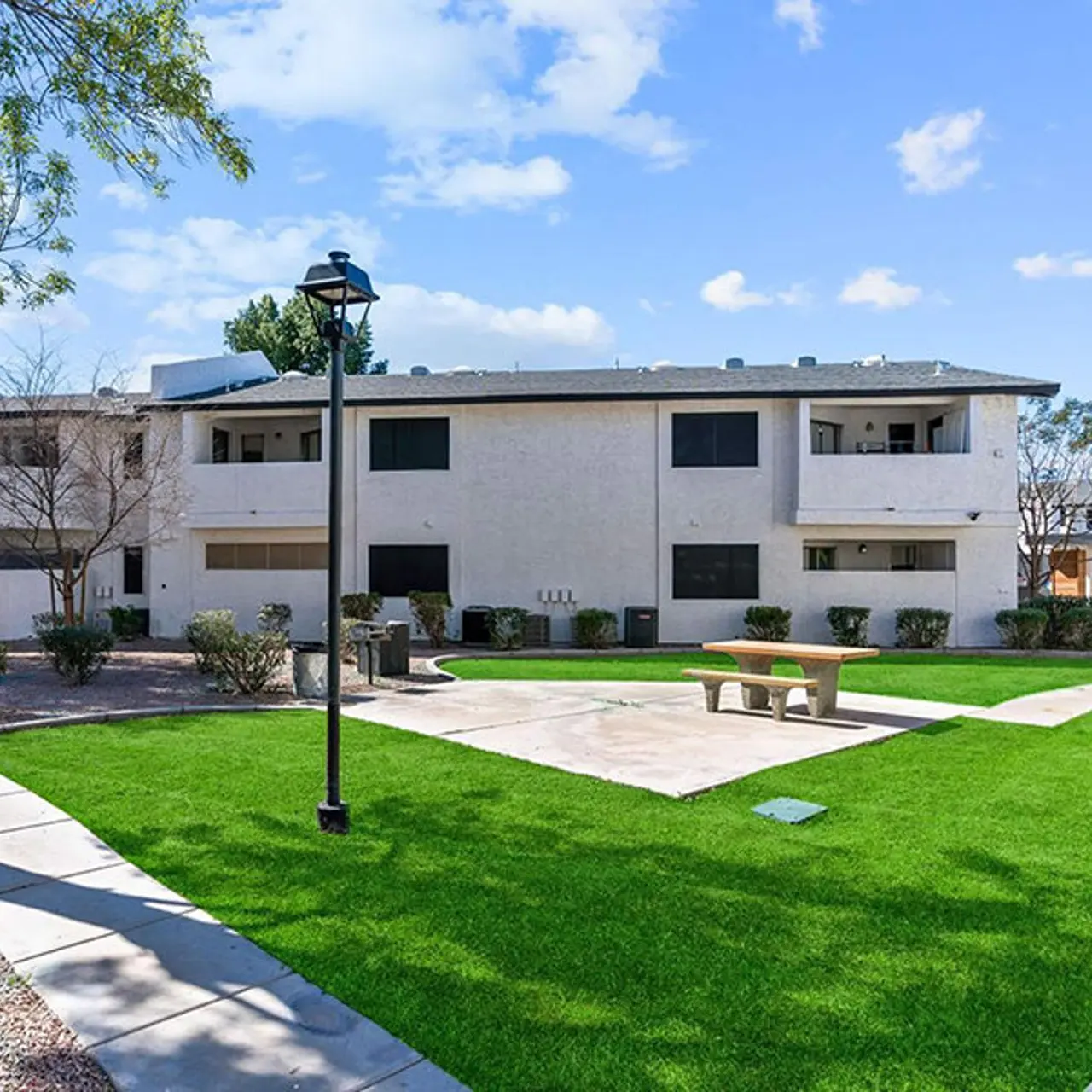Exterior view of a residential apartment complex with a green lawn and seating area.