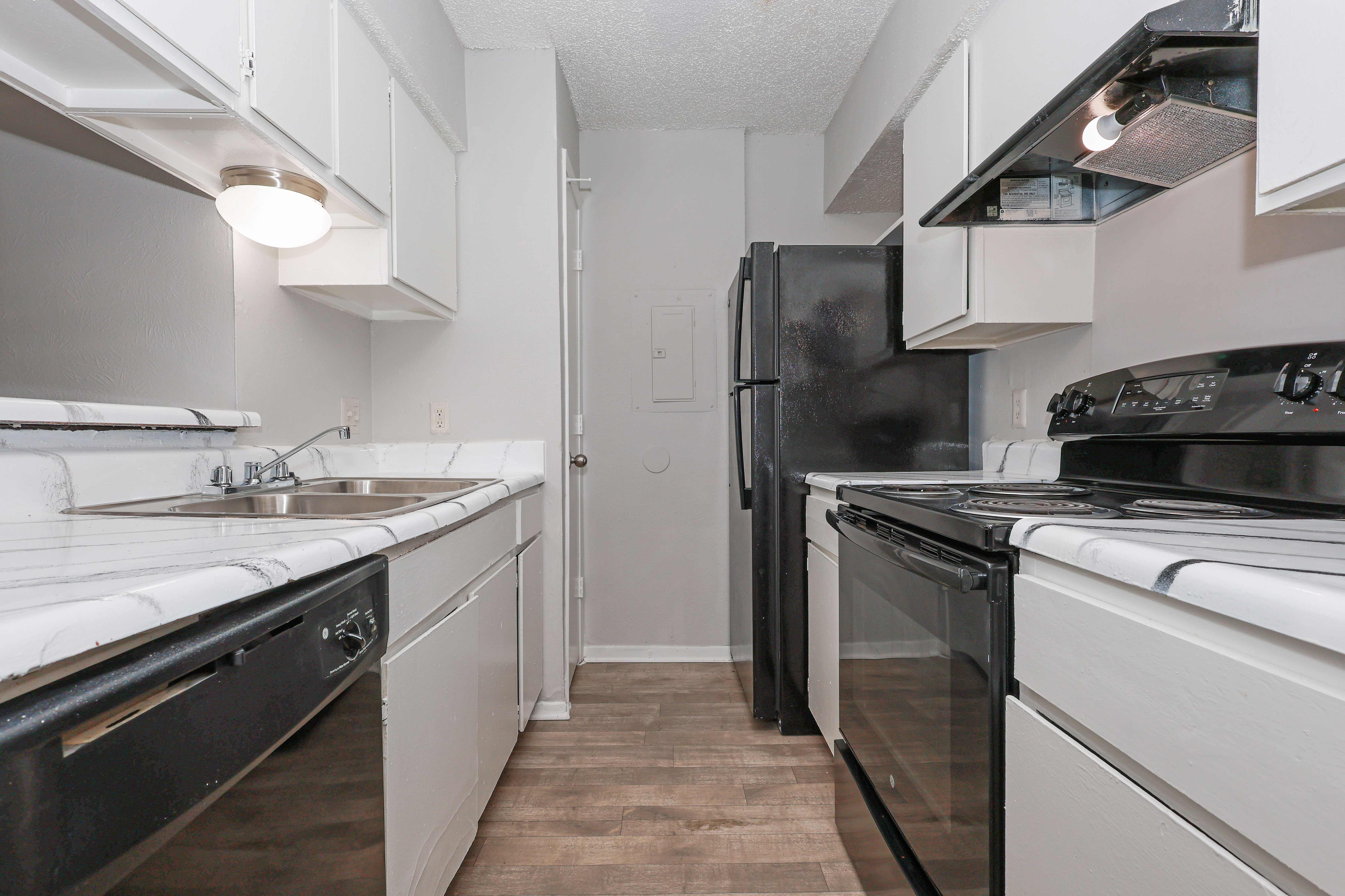 A modern kitchen featuring white cabinets, a black refrigerator, and dark appliances. The kitchen has a clean and organized layout with ample countertop space and a sink.