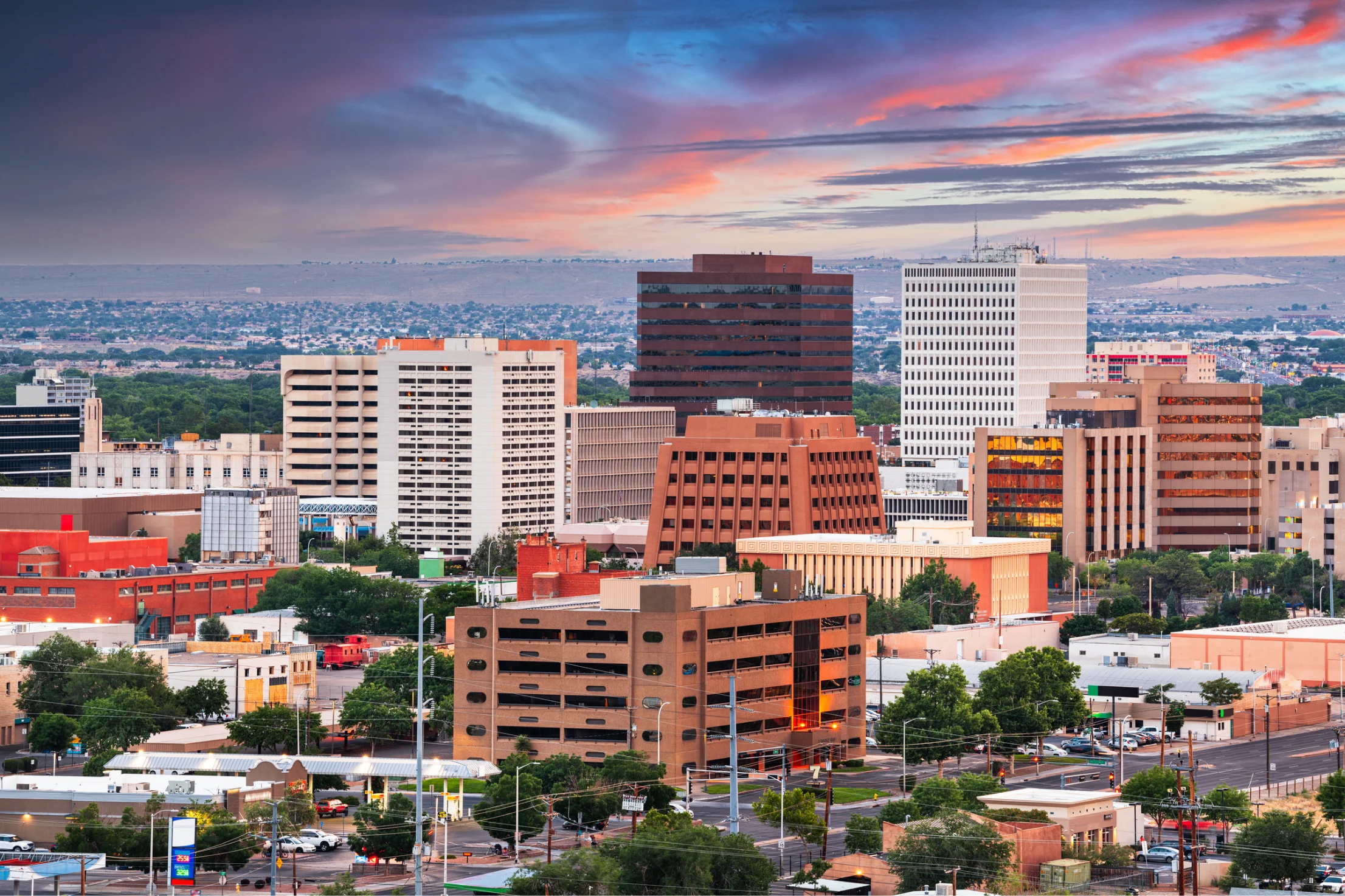 A panoramic view of a city skyline featuring a mix of modern and traditional architecture against a colorful sunset sky.