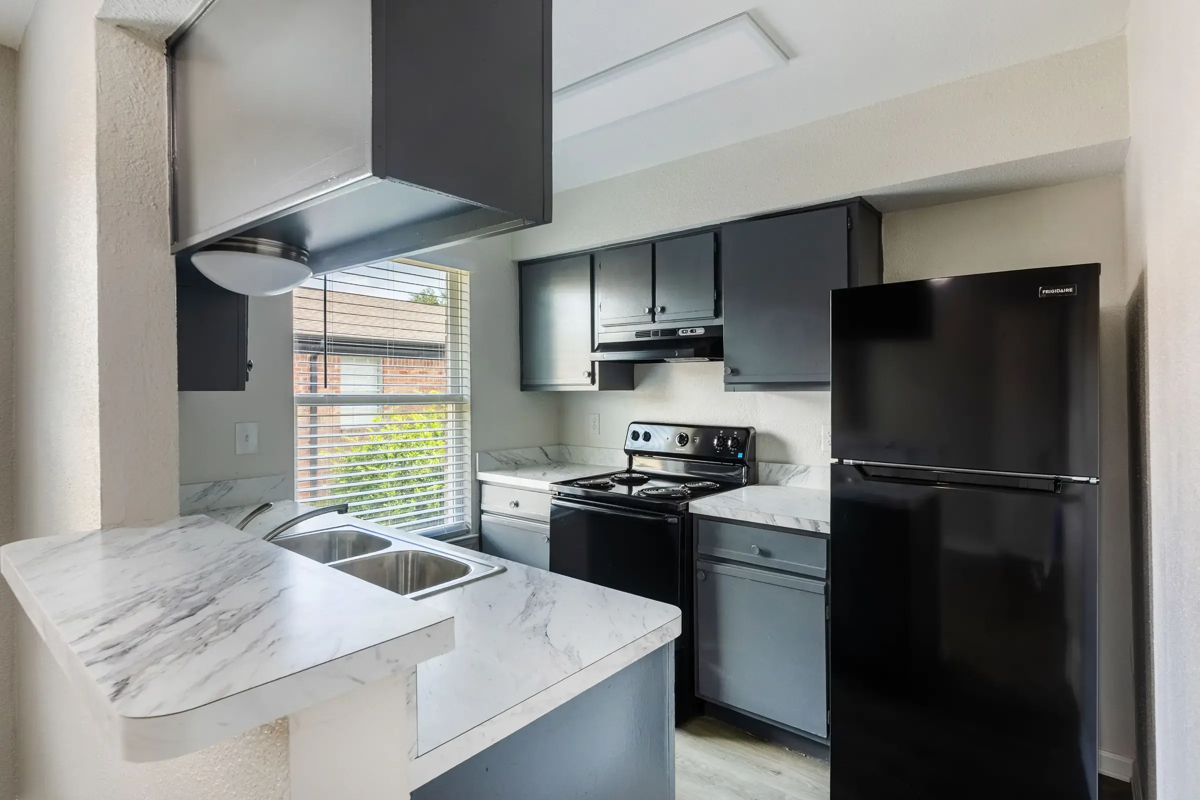 A modern kitchen featuring dark cabinetry, a black refrigerator, and a stove with a marble countertop.