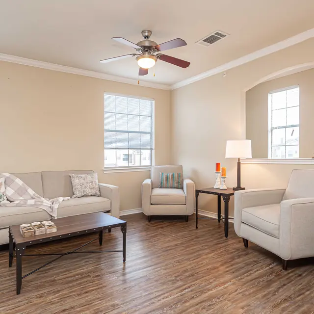 Inviting Living Room Interior A cozy living room with a fan, two armchairs, a sofa, and a coffee table on a wooden floor.