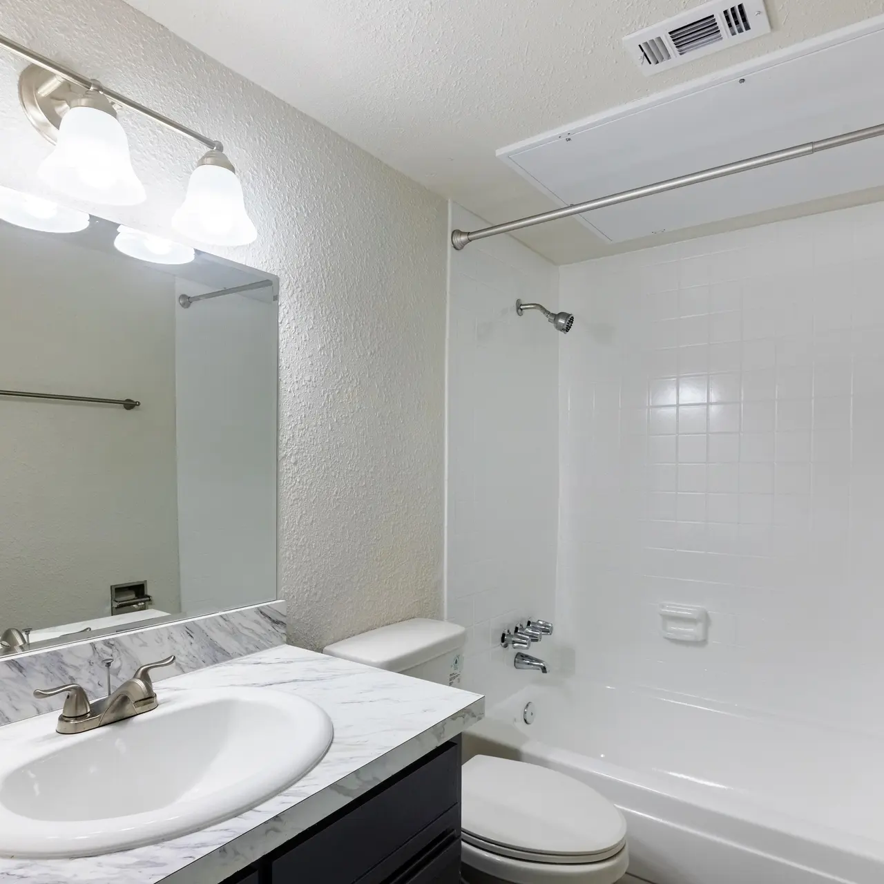 A modern bathroom featuring a white bathtub, marble sink countertop, and bright lighting. The walls are painted in a neutral tone, with a large mirror above the sink and a towel rack to the side.