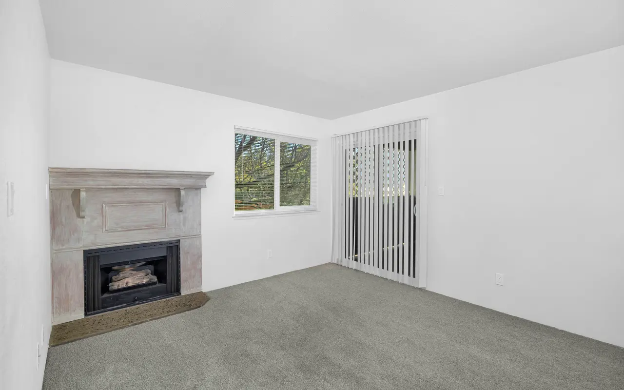 An empty living room featuring a fireplace, a large window with a view, and sliding glass doors.