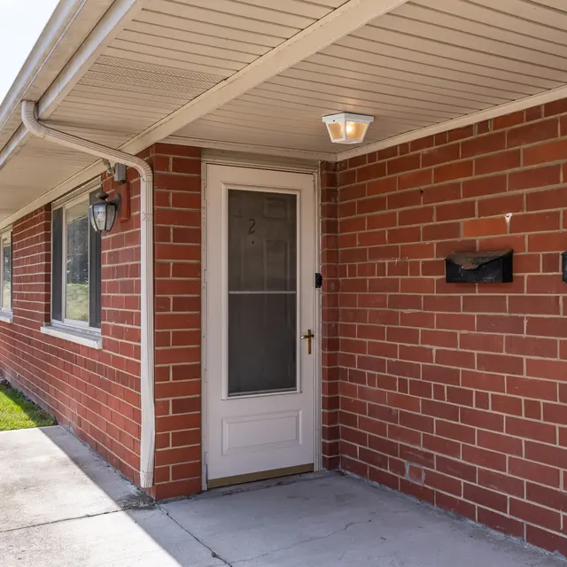 Brick Building Exterior Entryway Entryway of a brick building featuring a door with a glass panel, two light fixtures, and two mailboxes mounted on the wall.