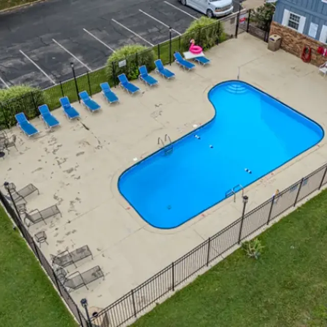 Aerial view of a swimming pool area with blue water, surrounded by green grass and lounge chairs.