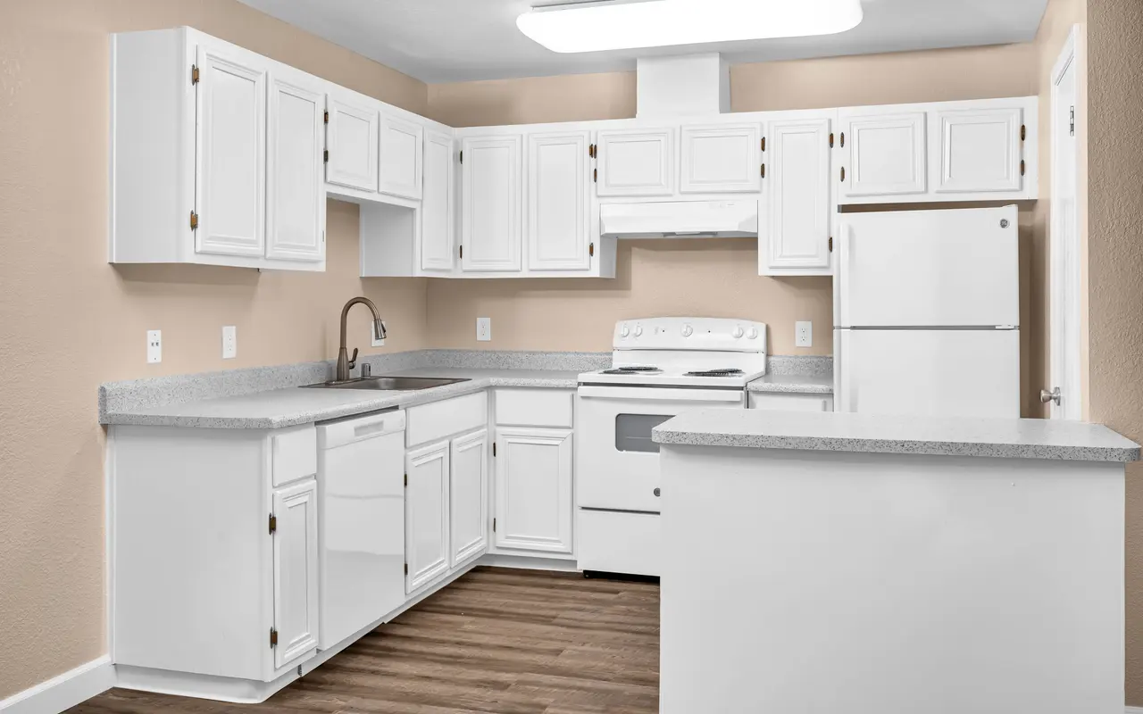A modern kitchen with white cabinets and appliances, featuring a grey countertop and wooden flooring.
