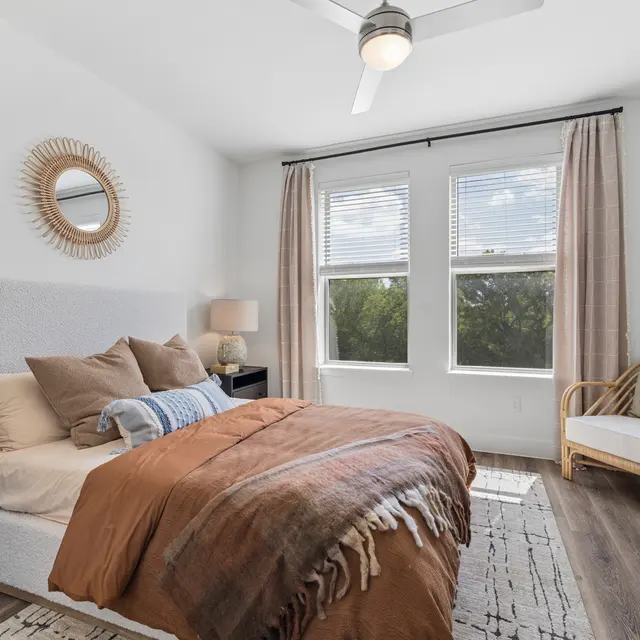Cozy Bedroom Retreat A cozy bedroom featuring a neatly made bed with pillows and a decorative blanket, large windows with natural light, and a stylish rattan chair.