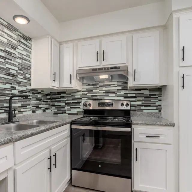 A modern kitchen featuring white cabinetry, stainless steel appliances, and a backsplash of small green and gray tiles.
