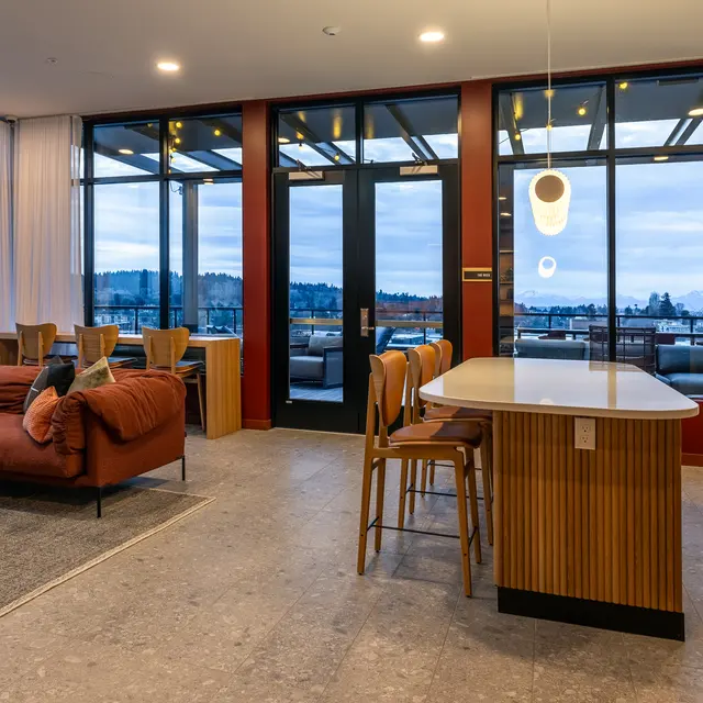 A modern living room and kitchen area featuring a coral-colored sofa, a sleek kitchen island, and large windows with a view of the outdoors.