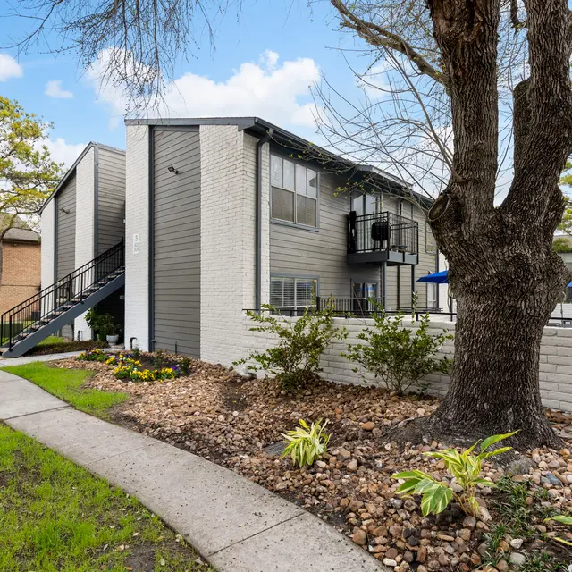 Apartment Complex Exterior Exterior view of an apartment complex featuring a two-story building with a landscaped pathway, trees, and garden beds in the foreground.