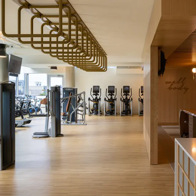 A spacious and modern gym interior featuring fitness equipment, hardwood flooring, and large windows with a city view.