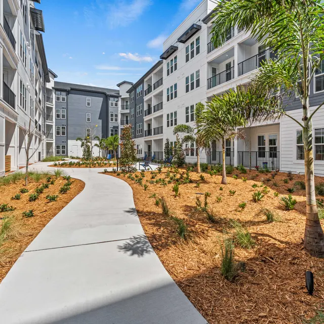 Landscaped Apartment Courtyard A landscaped courtyard in an apartment complex featuring a paved pathway, greenery, and modern architecture.