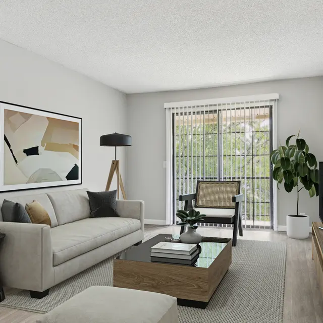 The Easton A modern living room featuring a light gray sofa with decorative pillows, a dark wood coffee table, and a small black side table. There is a floor lamp and an abstract artwork on the wall. Large windows with blinds allow natural light, and a potted plant is in the corner, adding a touch of greenery to the space.