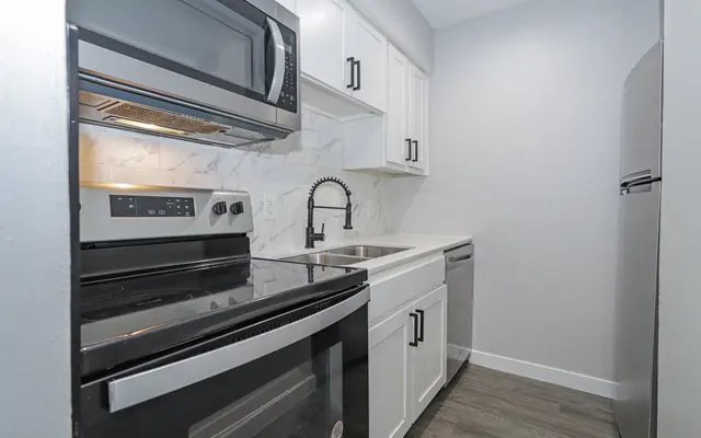 A modern kitchen featuring an oven, microwave, sink, and dishwasher, with white cabinets and gray walls.