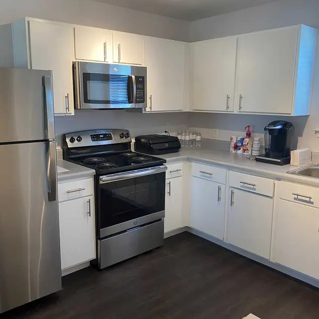 A modern kitchen featuring stainless steel appliances, including a refrigerator, stove, and microwave, with white cabinets and a sink near a window.