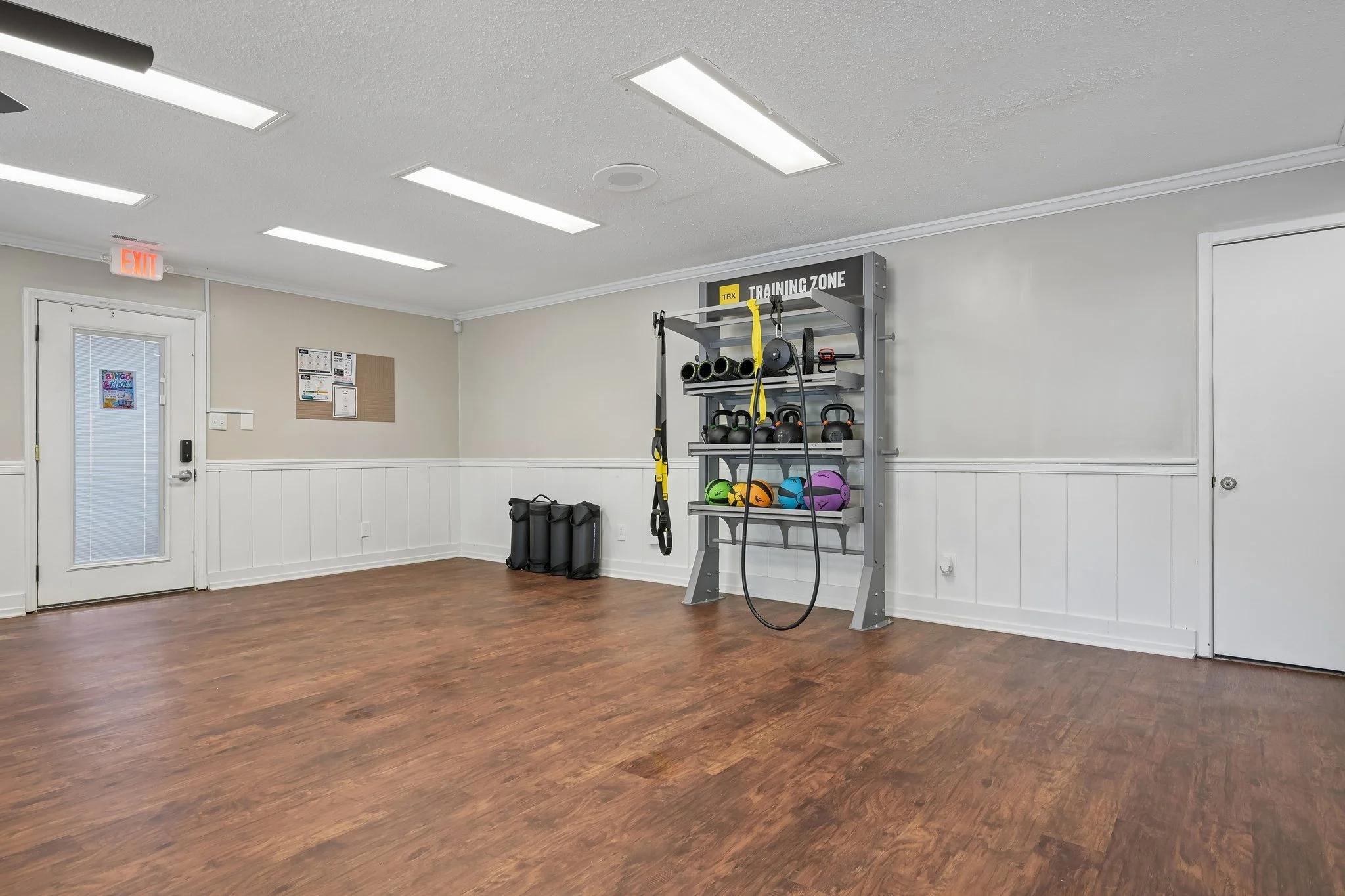 Interior view of a fitness room with storage for exercise equipment, wooden flooring, and bright lighting.