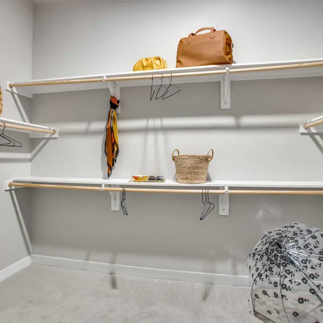 An organized closet with shelves displaying bags, baskets, and an umbrella on the floor.