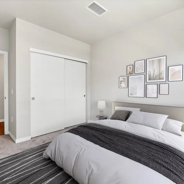 Modern Bedroom Interior A modern bedroom featuring a neatly made bed with white and gray bedding, a striped area rug, two bedside tables with lamps, and a wall adorned with framed artwork. There are closet doors and a doorway leading to another room.