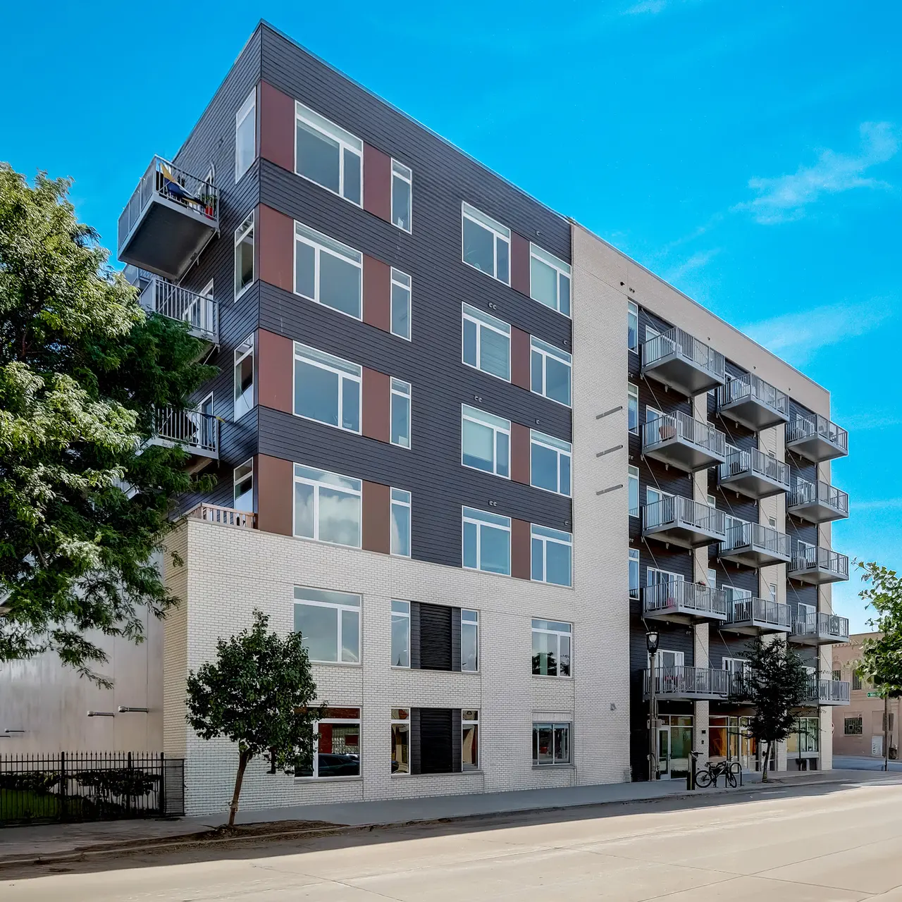 Modern Apartment Building A modern apartment building with balconies and large windows, surrounded by trees on a sunny day.