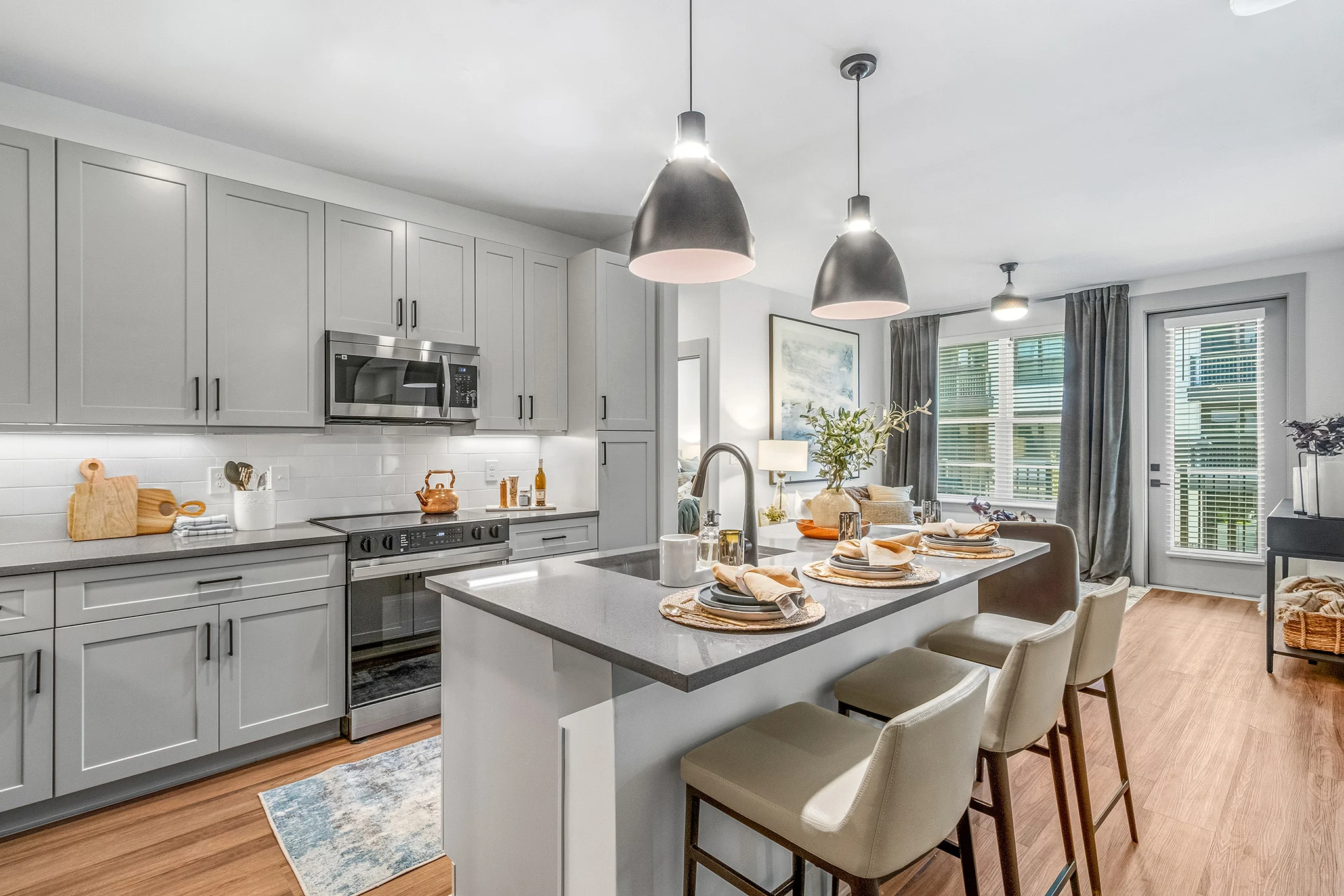 Stylish Modern Kitchen A modern kitchen featuring gray cabinetry, stainless steel appliances, and a large island with bar stools. Decor includes a vase of flowers and a rug on the floor.