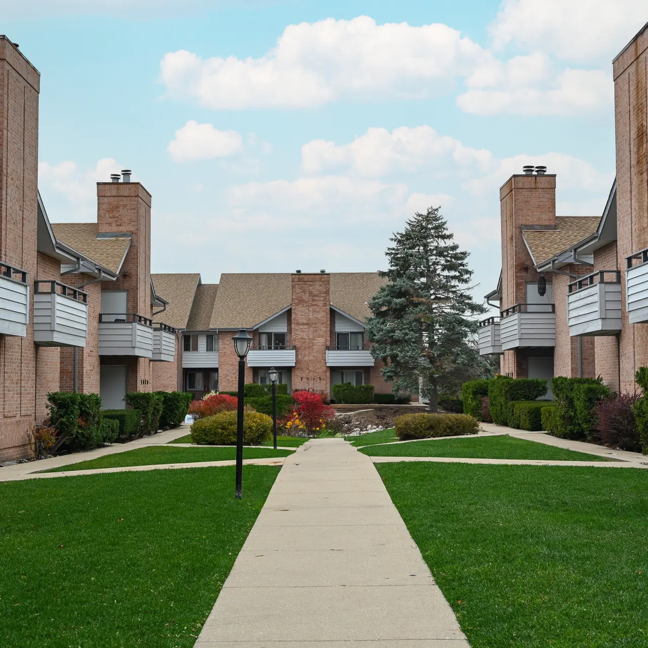 A landscaped walkway between apartment buildings with green lawns and bushes.