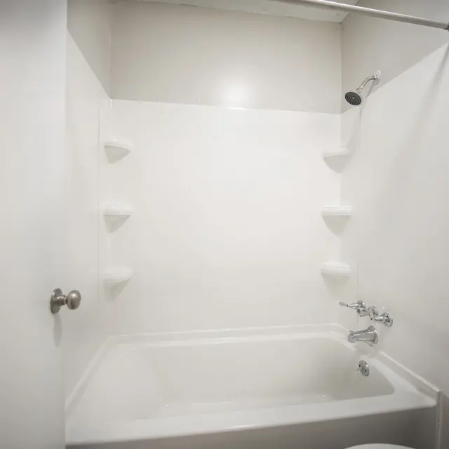 A clean, simple bathroom with a white bathtub and shower area, featuring a showerhead mounted on the wall and built-in shelves.