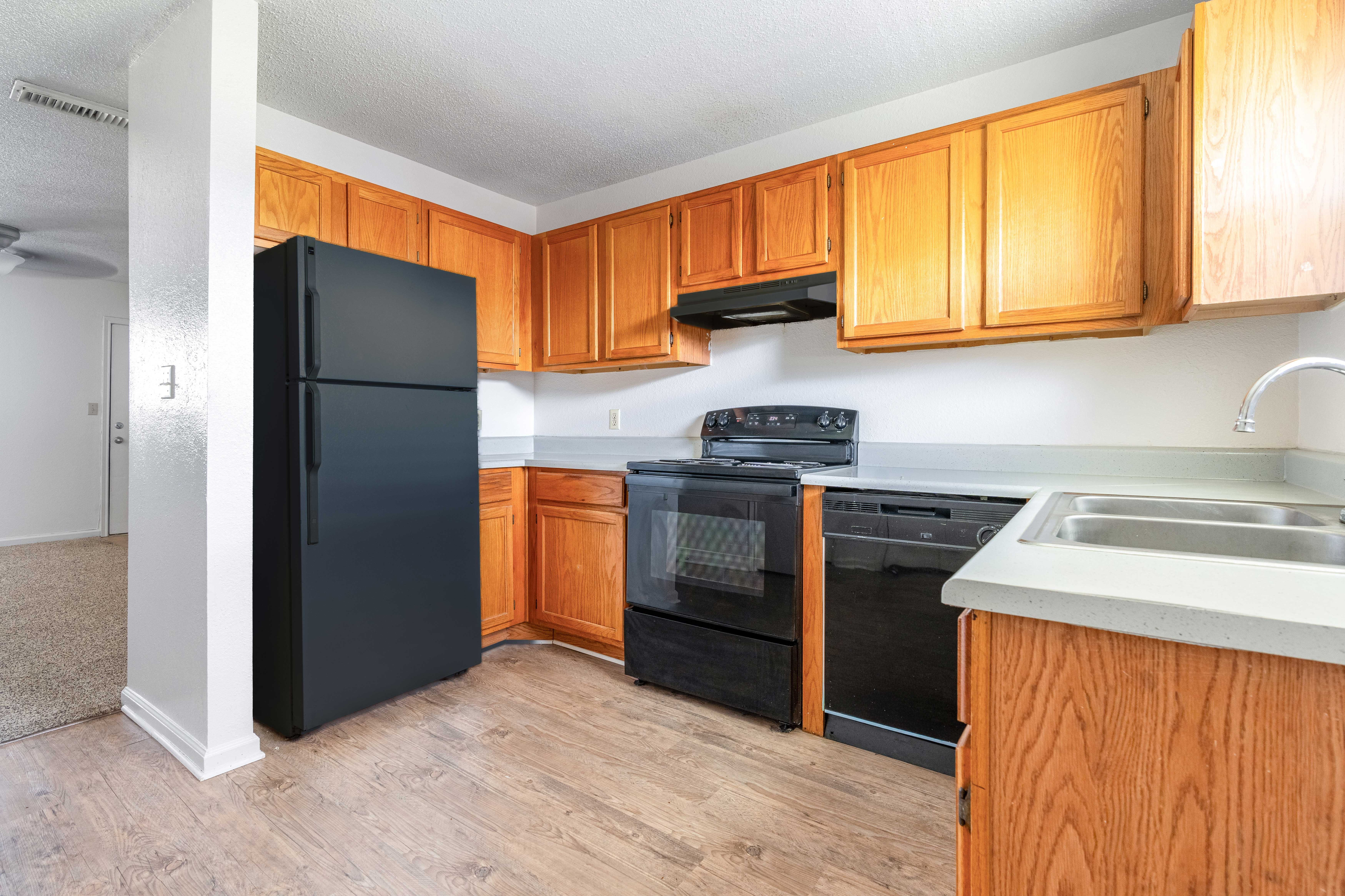 A modern kitchen featuring wooden cabinets, a black refrigerator, black stove, and a sink with a countertop.