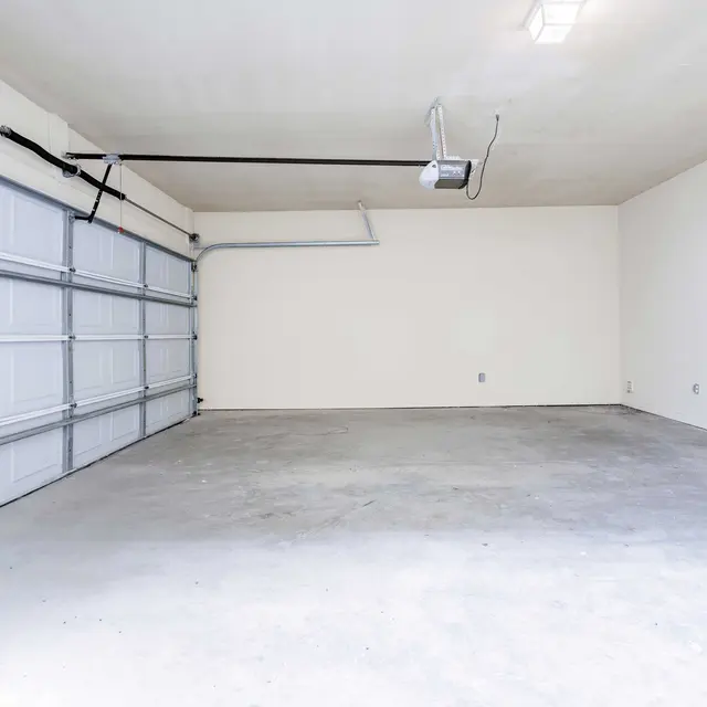 An empty garage space with a white painted concrete floor and a large garage door along one wall.