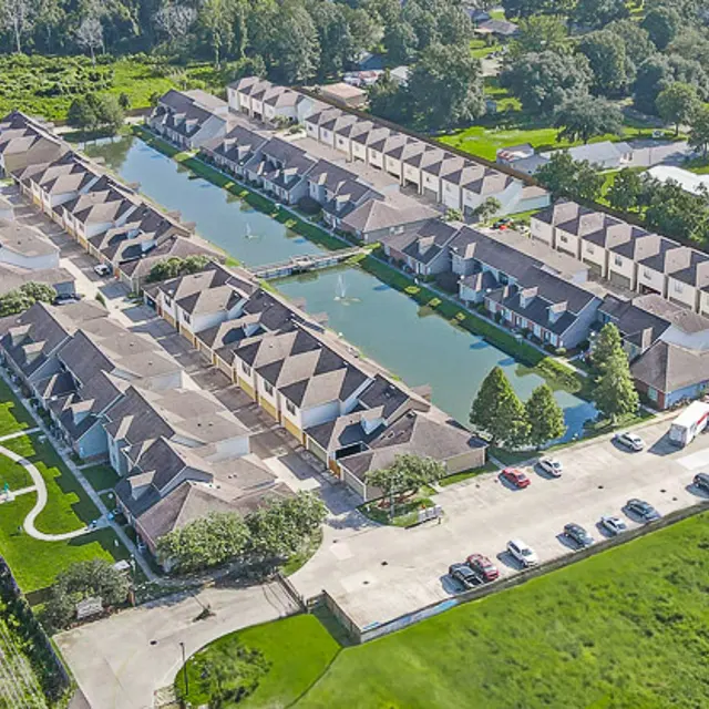 Aerial view of a residential area featuring townhouses arranged along a waterway, surrounded by green lawns and trees.