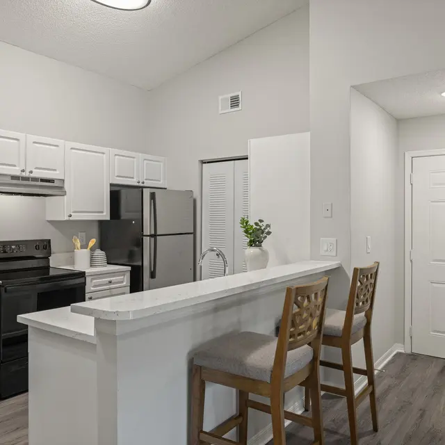 A modern kitchen featuring white cabinetry, stainless steel appliances, and a breakfast bar with two stools.