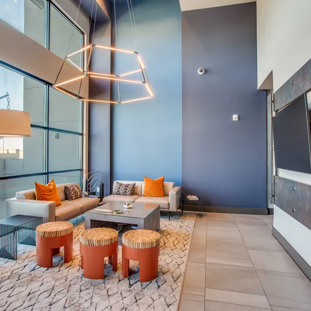 A stylish modern living room with large windows, a contemporary lighting fixture, a comfortable seating arrangement, and decorative stools.