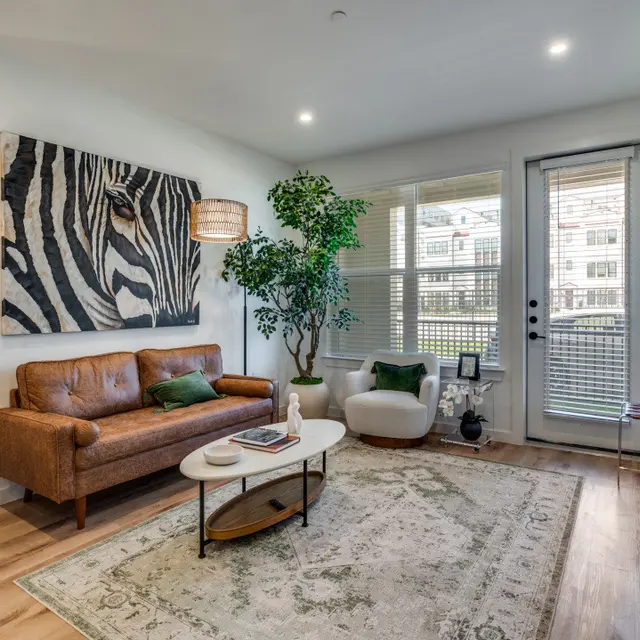 A modern living room featuring a leather sofa, a large zebra artwork on the wall, indoor plants, and a glass door leading to an outdoor area.