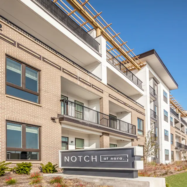 Exterior view of a modern apartment complex named Notch at Nora, showcasing brick architecture and balconies under a clear blue sky.