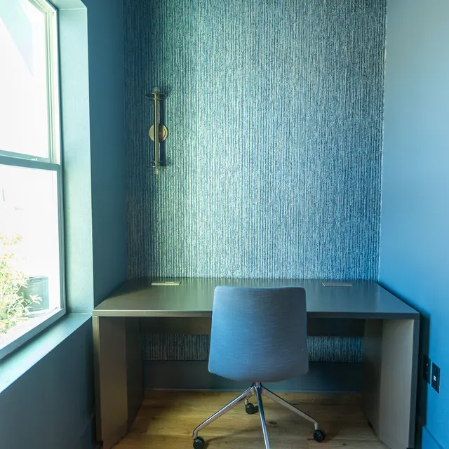 A modern workspace designed in a corner with a desk and chair, natural light coming through a window, and a patterned wall.