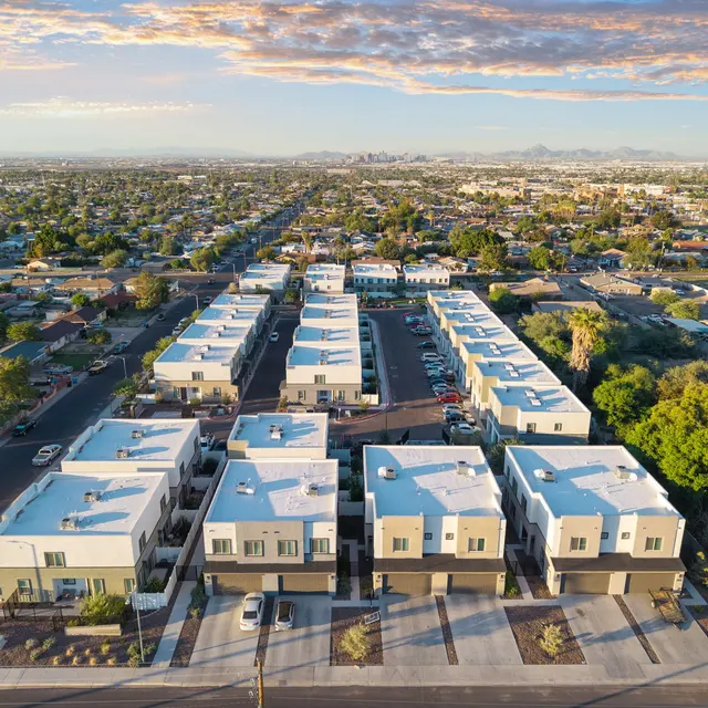 Aerial View of a Modern Housing Development Aerial view of a modern housing development with multiple white-roofed buildings arranged in neat rows, surrounded by green trees and a suburban landscape.