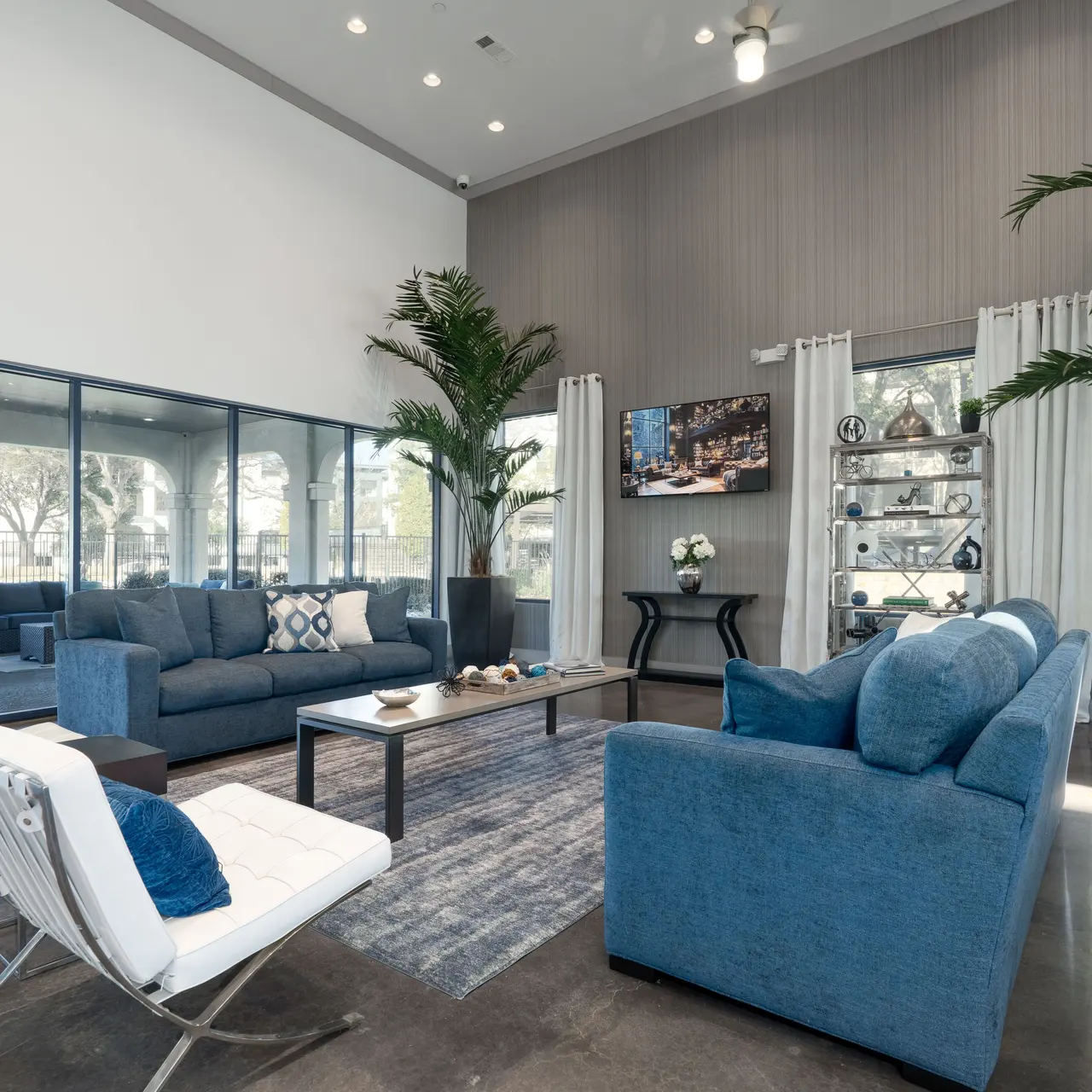 Clubhouse A modern living room with blue sofas, white chairs, and large windows letting in light.