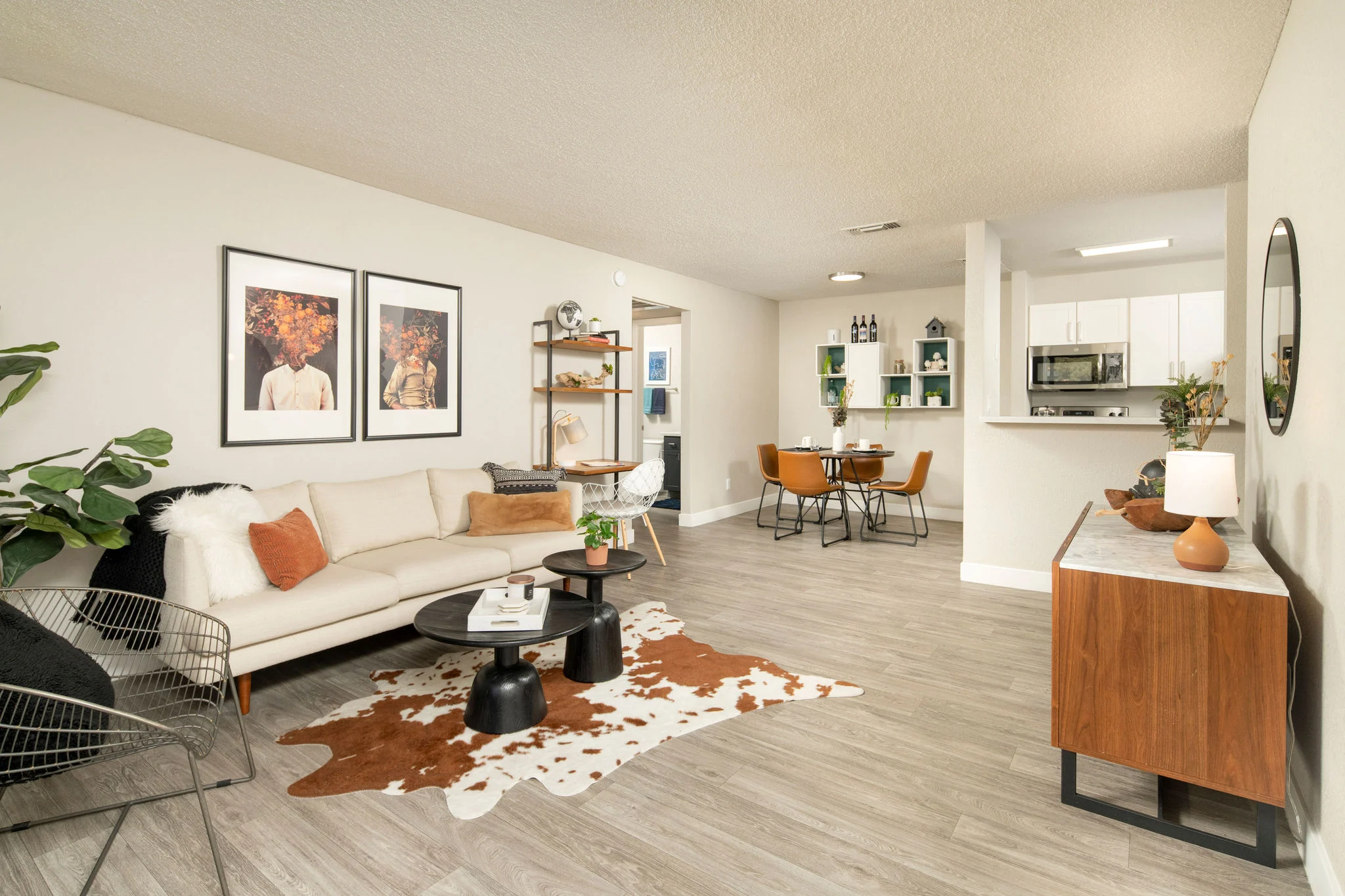 Modern Living Room Interior Spacious modern living room with a light-colored couch, coffee table, and decorative elements. There are framed artworks on the wall, a dining area with a round table and chairs, and an open kitchen in the background.