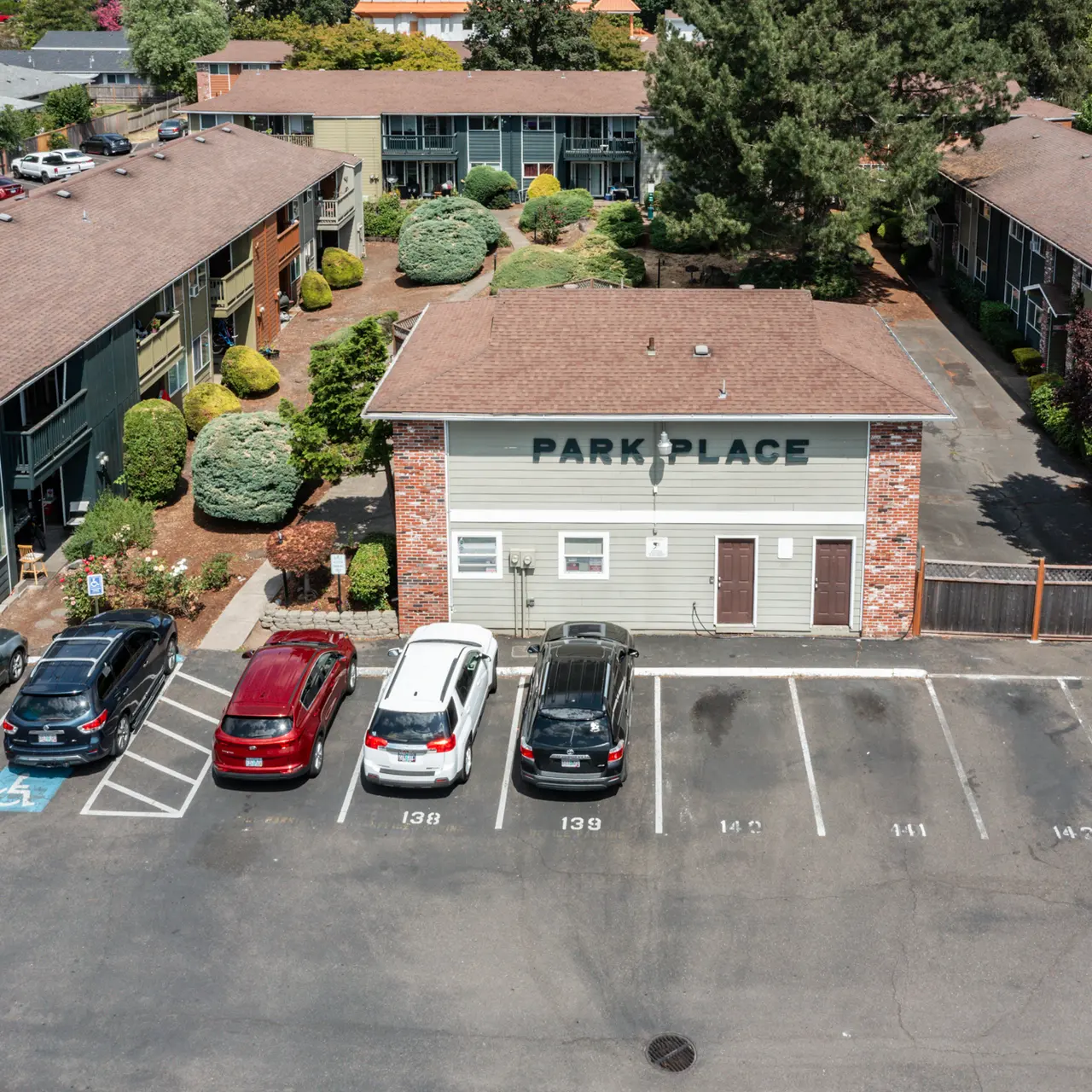 Park Place Apartment Complex Aerial view of an apartment complex named Park Place, featuring multiple buildings with brown roofs, landscaped areas, and a parking lot filled with cars.