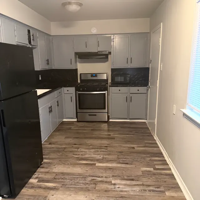 An interior view of a modern kitchen featuring gray cabinets, black appliances, and wooden flooring.